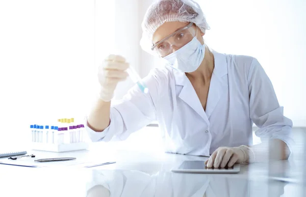 Cientista profissional em óculos de proteção pesquisando tubo com reagentes em laboratório ensolarado. Medicina e investigação científica — Fotografia de Stock