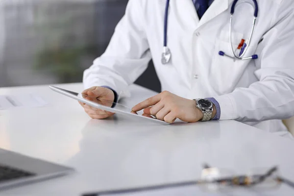 Médico masculino desconocido sentado y trabajando con Tablet PC en la clínica en su lugar de trabajo, primer plano. Médico joven en el trabajo. Servicio médico perfecto, concepto de medicina — Foto de Stock