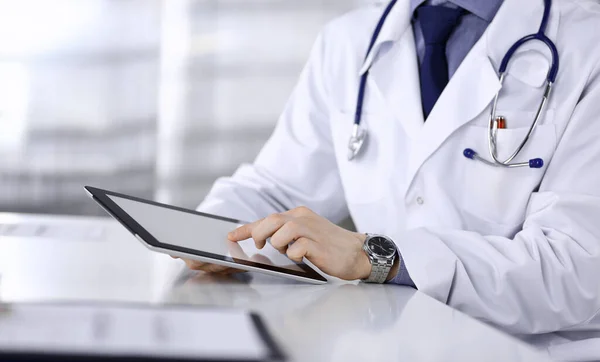 Médico masculino desconocido sentado y trabajando con Tablet PC en la clínica en su lugar de trabajo, primer plano. Médico joven en el trabajo. Servicio médico perfecto, concepto de medicina — Foto de Stock