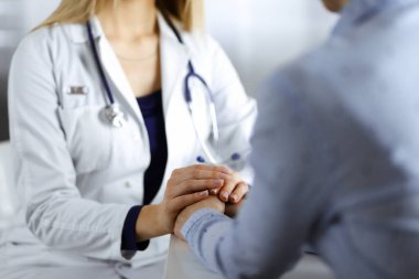 Bilinmeyen kadın-doktor, klinikteki dolapta yan yana otururken hastaya güven vermek için hastasının elini tutuyor ve mevcut sağlık muayenesini tartışıyor. Kadın.