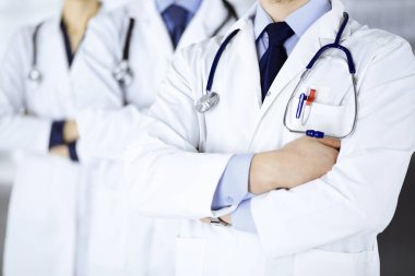 Hastane ofisinde çapraz kolları ve steteskopları olan bir grup modern doktor bir takım gibi duruyor. Doktorlar hastaları muayene etmeye ve yardım etmeye hazır. Tıbbi yardım, sağlık sigortası, en iyi hastalık