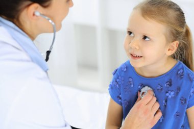 Doktor steteskopla küçük bir kızı muayene ediyor. Her zamanki tıbbi muayenede gülümseyen çocuk hasta. Tıp ve sağlık hizmetleri kavramları