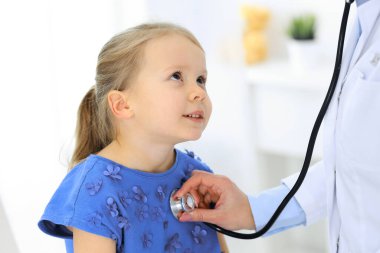 Doktor steteskopla küçük bir kızı muayene ediyor. Her zamanki tıbbi muayenede gülümseyen çocuk hasta. Tıp ve sağlık hizmetleri kavramları