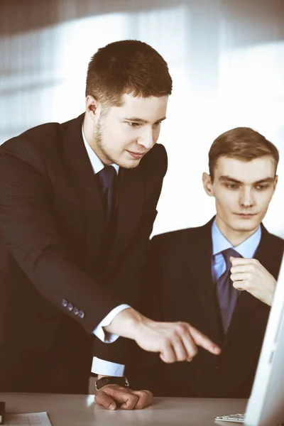 Two businessmen discussing questions at meeting in a modern office, using a computer. Headshot at negotiation or workplace. Teamwork, partnership and business concept