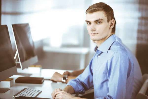 Deux jeunes hommes d'affaires confiants, assis au bureau dans un bureau moderne, tout en travaillant sur les ordinateurs sur leur nouveau projet. Le travail d'équipe en entreprise comme concept de réussite de nos jours — Photo