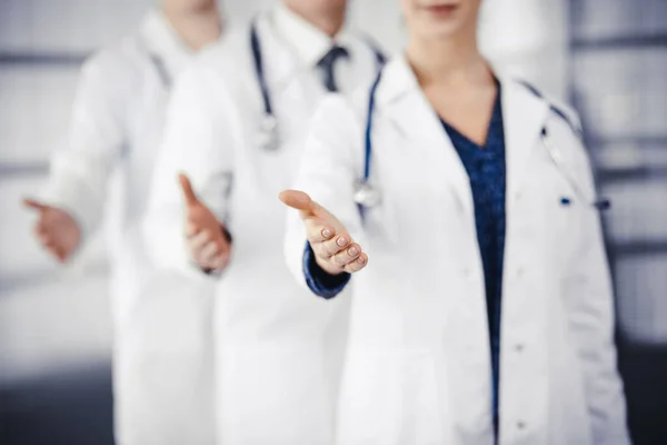 Artsen staan als een team, terwijl het aanbieden van helpende hand voor het schudden van de hand of het redden van leven in de kliniek — Stockfoto