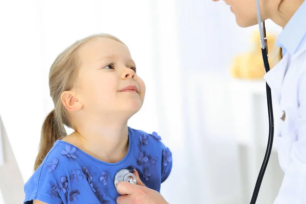 Arzt untersucht ein kleines Mädchen per Stethoskop. Glücklich lächelnder Kinderpatient bei der üblichen ärztlichen Untersuchung. Medizin- und Gesundheitskonzepte — Stockfoto