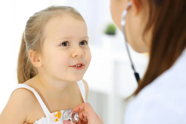 Доктор осматривает маленькую девочку стетоскопом. Счастливого улыбающегося ребенка при обычном медицинском осмотре. Медицина и здравоохранение — стоковое фото