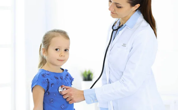 Arzt untersucht ein kleines Mädchen per Stethoskop. Glücklich lächelnder Kinderpatient bei der üblichen ärztlichen Untersuchung. Medizin- und Gesundheitskonzepte — Stockfoto