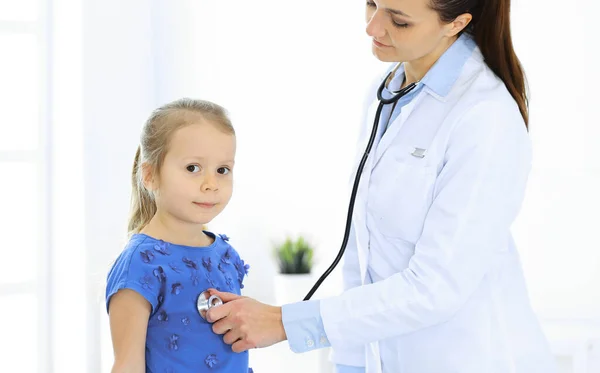 Doctor examining a little girl by stethoscope. Happy smiling child patient at usual medical inspection. Medicine and healthcare concepts Royalty Free Stock Photos