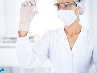 Koruyucu gözlüklü profesyonel kadın bilim adamı laboratuarda reaktörlerle araştırma tüpü kullanıyor. Tıp ve bilim araştırmaları kavramları