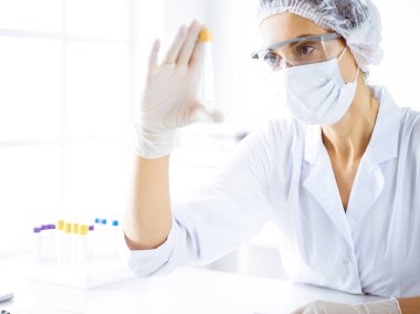 Koruyucu gözlüklü profesyonel kadın bilim adamı laboratuarda reaktörlerle araştırma tüpü kullanıyor. Tıp ve bilim araştırmaları kavramları