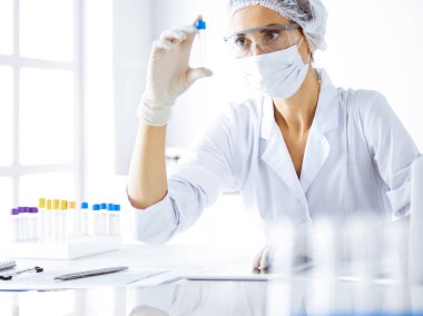 Koruyucu gözlüklü profesyonel kadın bilim adamı laboratuarda reaktörlerle araştırma tüpü kullanıyor. Tıp ve bilim araştırmaları kavramları