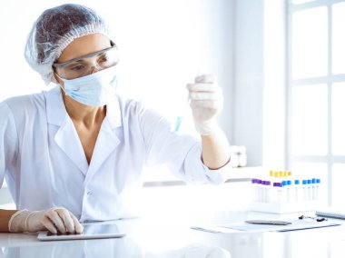 Koruyucu gözlüklü profesyonel kadın bilim adamı laboratuarda reaktörlerle araştırma tüpü kullanıyor. Tıp ve bilim araştırmaları kavramları