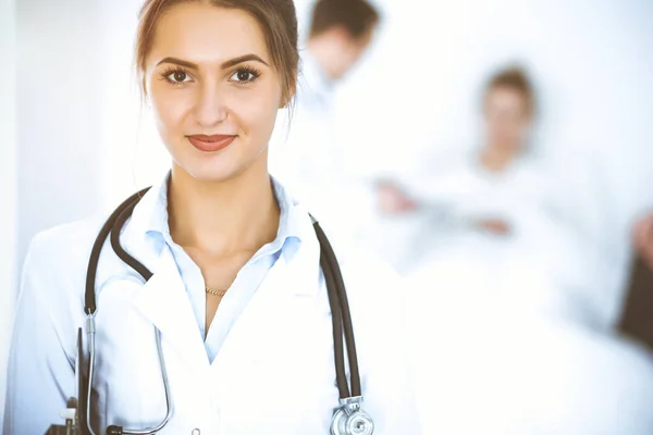 Doctora sonriendo en el fondo con paciente en la cama y dos doctores — Foto de Stock