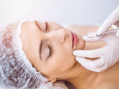 Güzellik uzmanı güneşli spa merkezinde genç esmer bir kadının yüzüne şırıngayla güzellik prosedürü uyguluyor. Kozmetik ilaç ve ameliyat, güzellik iğneleri.