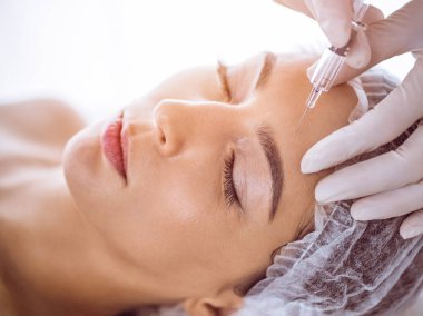 Güzellik uzmanı güneşli spa merkezinde genç esmer bir kadının yüzüne şırıngayla güzellik prosedürü uyguluyor. Kozmetik ilaç ve ameliyat, güzellik iğneleri.