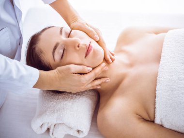 Güzel esmer kadın güneşli spa merkezinde gözleri kapalı yüz masajından hoşlanıyor. Rahatlatıcı tedavi ve kozmetik tıp kavramları