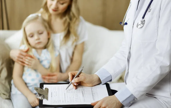 Doctor and patient. Pediatrician using clipboard while examining little girl with her mother at home. Sick and unhappy child at medical exam. Medicine concept — Stock Photo, Image
