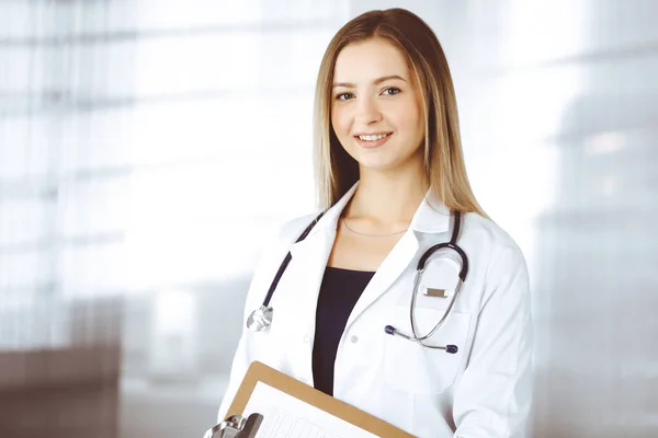Молодая оптимистичная женщина-врач держит планшет в руках, стоя в клинике. Портрет дружелюбной женщины-врача со стетоскопом. Идеальное медицинское обслуживание в больнице. Медицина — стоковое фото