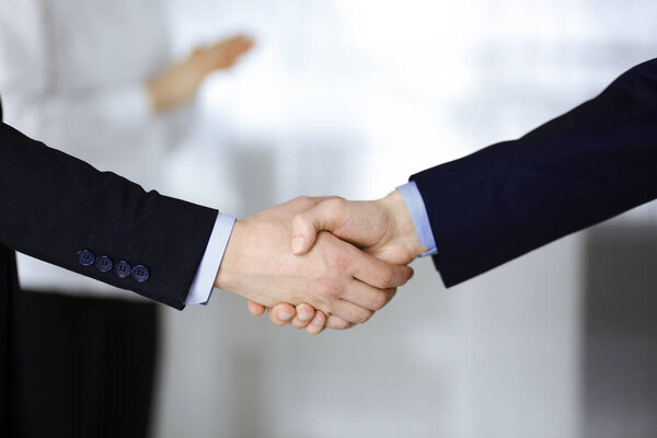 Business people shaking hands at meeting or negotiation, close-up. Group of unknown businessmen and a woman standing in a modern office. Teamwork, partnership and handshake concept