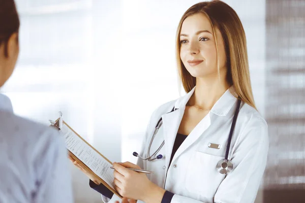 La jeune femme-médecin et sa patiente discutent de l'examen de santé actuel des patients, tout en restant ensemble dans un bureau d'hôpital. Une femme médecin écrit des marques à l'aide d'un presse-papiers. Parfait. — Photo