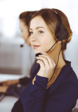 İki iş kadını, modern bir ofiste masada otururken müşterilerle kulaklıkla sohbet ediyorlar. Çağrı merkezinde çeşitli insanlar. Tele pazarlama ve müşteri hizmetleri