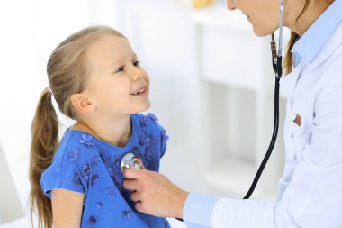 Doktor steteskopla küçük bir kızı muayene ediyor. Her zamanki tıbbi muayenede gülümseyen çocuk hasta. Tıp ve sağlık hizmetleri kavramları