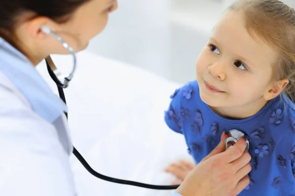 Arzt untersucht ein kleines Mädchen per Stethoskop. Glücklich lächelnder Kinderpatient bei der üblichen ärztlichen Untersuchung. Medizin- und Gesundheitskonzepte — Stockfoto