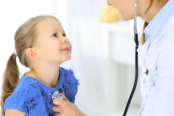 Arzt untersucht ein kleines Mädchen per Stethoskop. Glücklich lächelnder Kinderpatient bei der üblichen ärztlichen Untersuchung. Medizin- und Gesundheitskonzepte — Stockfoto