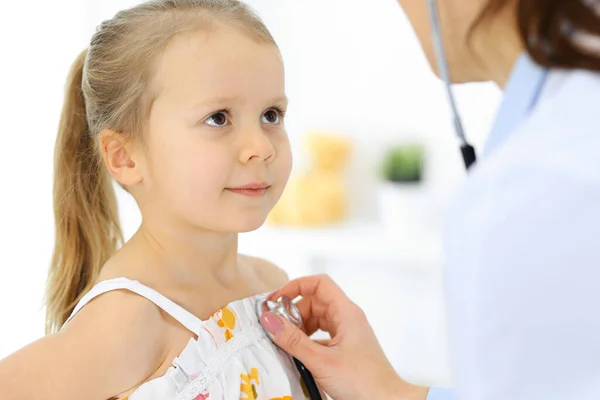 Doctor examinando a una niña por estetoscopio. Feliz niño sonriente paciente en la inspección médica habitual. Medicina y conceptos sanitarios — Foto de Stock