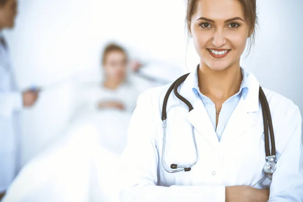 Female doctor smiling on the background with patient in the bed and two doctors