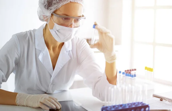 Cientista profissional em óculos de proteção pesquisando tubo com reagentes em laboratório ensolarado. Medicina e pesquisa — Fotografia de Stock