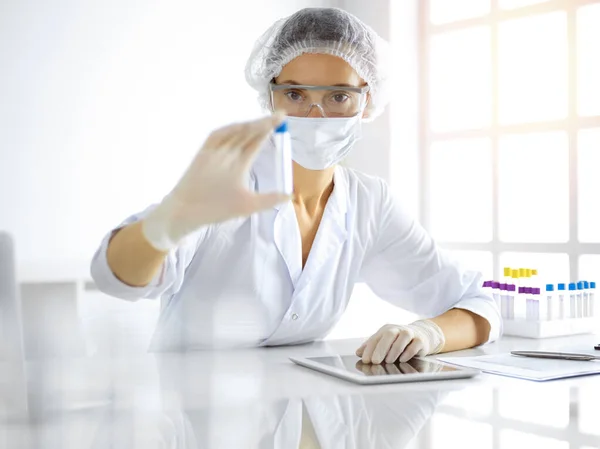 Científica profesional en gafas protectoras investigando tubo con reactivos en laboratorio soleado. Medicina e investigación — Foto de Stock