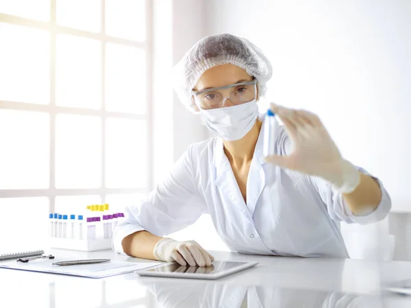 Científica profesional en gafas protectoras investigando tubo con reactivos en laboratorio soleado. Medicina e investigación — Foto de Stock