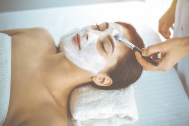 Güzel esmer kadın kapalı gözlerle kozmetik maske takmaktan zevk alıyor. Tıp ve kaplıca kavramlarında rahatlatıcı tedavi