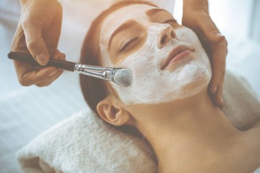 Güzel esmer kadın kapalı gözlerle kozmetik maske takmaktan zevk alıyor. Tıp ve kaplıca kavramlarında rahatlatıcı tedavi