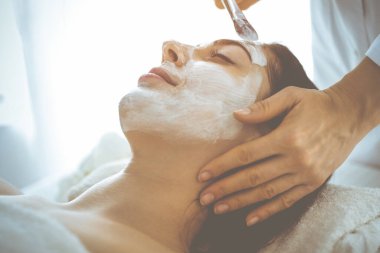 Güzel esmer kadın kapalı gözlerle kozmetik maske takmaktan zevk alıyor. Tıp ve kaplıca kavramlarında rahatlatıcı tedavi