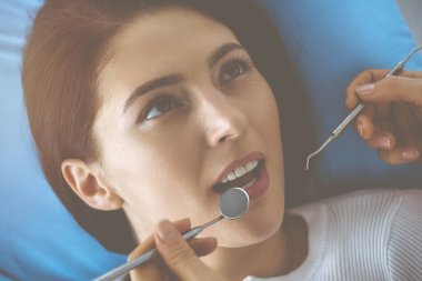 Gülümseyen esmer kadın diş hekimi tarafından muayene ediliyor. Hastanın ağzının yanında diş aletleri tutan bir doktorun elleri. Sağlıklı diş ve ilaç konsepti