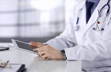 Bilinmeyen erkek doktor klinikteki tablet bilgisayarla yakın planda çalışıyor. İşteki genç doktor. Mükemmel sağlık hizmeti, tıp konsepti