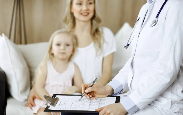 Doctor and patient. Pediatrician using clipboard while examining little girl with her mother at home. Happy cute caucasian child at medical exam. Medicine concept — Stock Photo, Image