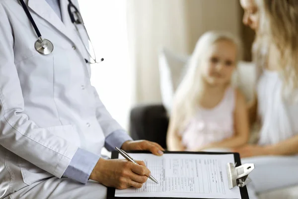 Doctor y paciente. Pediatra usando portapapeles mientras examina a la niña con su madre en casa. Niña enferma e infeliz en el examen médico. Concepto de medicina — Foto de Stock