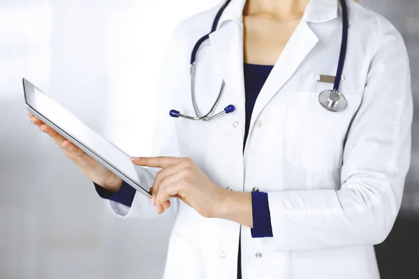 Neznámá žena-doktorka drží v rukou tablet, zatímco stojí na klinice. Ženský lékař se stetoskopem v její kanceláři, detailní záběr. Perfektní lékařská služba v nemocnici. Medicína — Stock fotografie