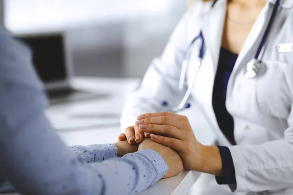 Bilinmeyen kadın-doktor, klinikteki dolapta otururken hastalarının ellerini tutuyor ve mevcut sağlık muayenesini tartışıyor. Steteskoplu bir doktor iş yerinde, yakın plan.