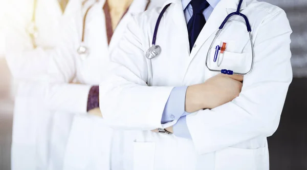 Group of modern doctors standing as a team with crossed arms and stethoscopes in a sunny hospital office. Physicians ready to examine and help patients. Medical help, insurance in health care, best — Stock Photo, Image