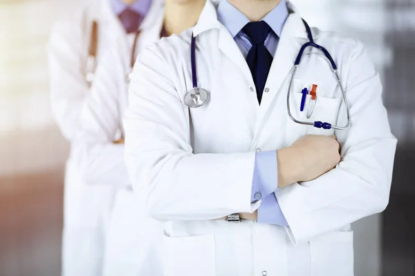 Grupp av moderna läkare står som ett team med korsade armar och stetoskop i en solig sjukhus kontor. Läkare redo att undersöka och hjälpa patienter. Medicinsk hjälp, sjukförsäkring, bäst — Stockfoto
