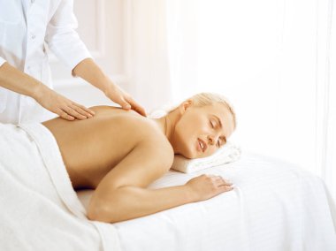Güzel sarışın kadın güneşli spa salonunda kapalı gözlerle sırt masajından hoşlanıyor. Güzellik konsepti