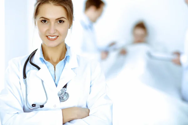Medico femminile sorridente sullo sfondo con paziente nel letto e due medici — Foto Stock