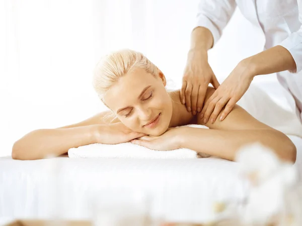 Vacker blond kvinna njuter av ryggmassage med slutna ögon i solig spa salong. Skönhetsbegreppet — Stockfoto