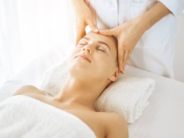 Güzel sarışın kadın güneşli spa merkezinde kapalı gözlerle yüz masajından hoşlanıyor. Tıp ve güzellik kavramlarında rahatlatıcı tedavi